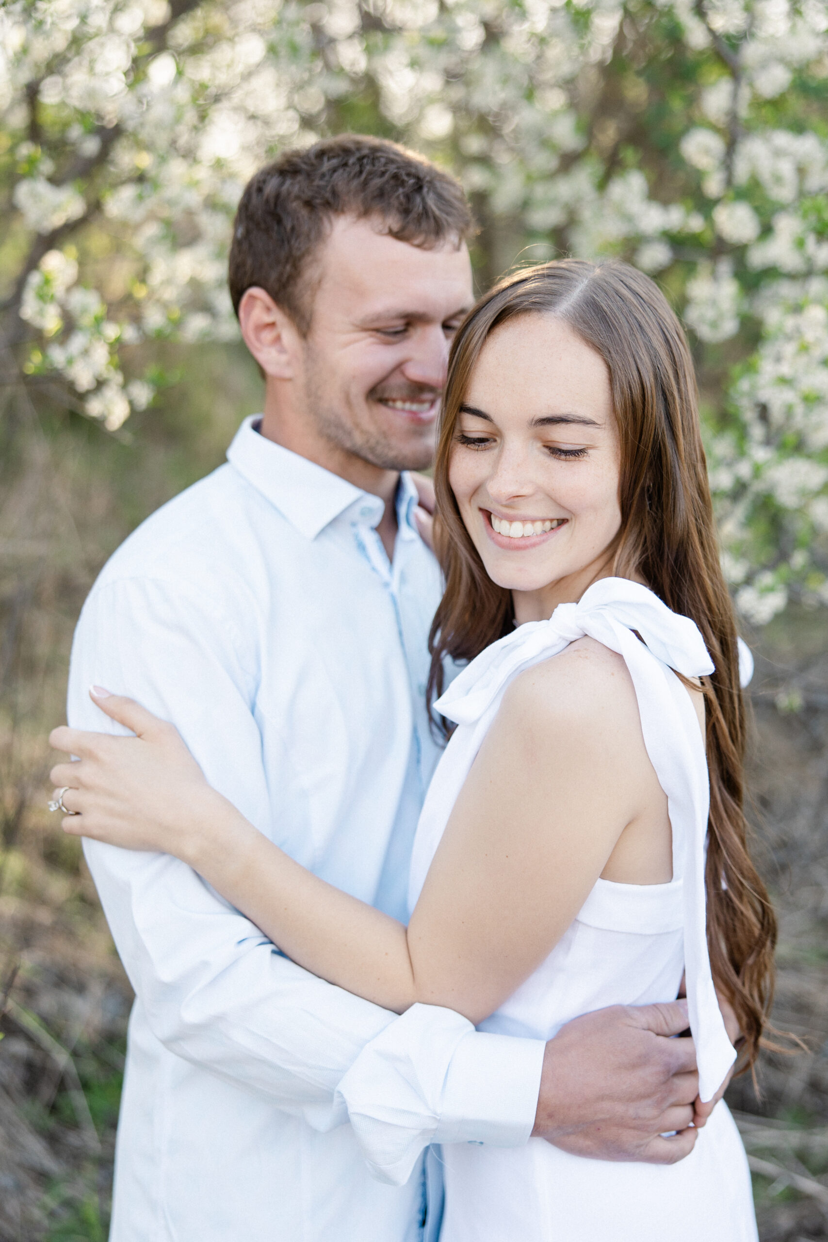 Kaitlyn and Connor standing under blooming white trees during a spring engagement session at Mary Jo Wegner Arboretum in Sioux Falls, SD.